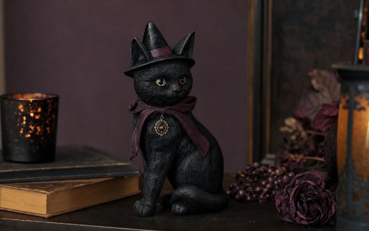 A black cat figurine in a witch hat beside stacked books and a candle lantern
