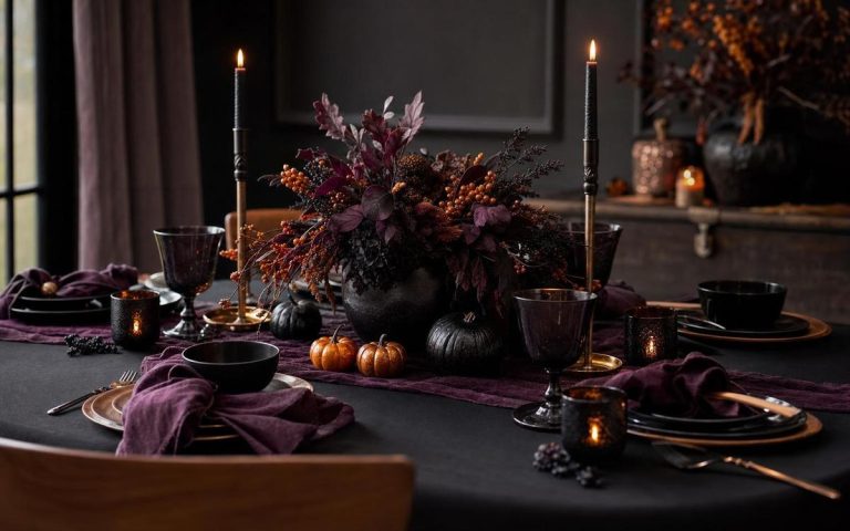 A candlelit Halloween table set with black dinnerware, purple linens, pumpkins and dark flowers
