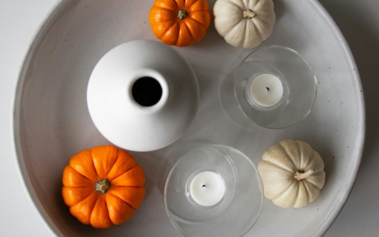 White tray styled with orange and cream mini pumpkins, a white vase and glass candle holders
