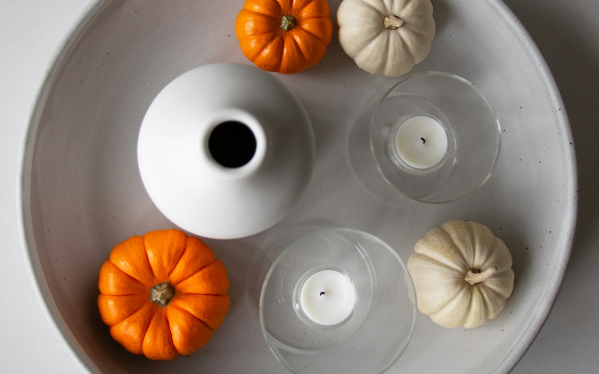 White tray styled with orange and cream mini pumpkins, a white vase and glass candle holders