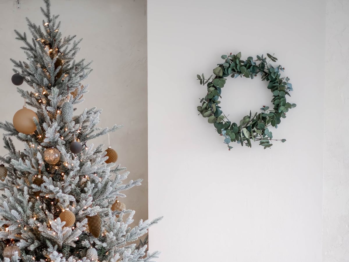 A frosted Christmas tree, eucalyptus wreath and wrapped gifts in a neutral living room