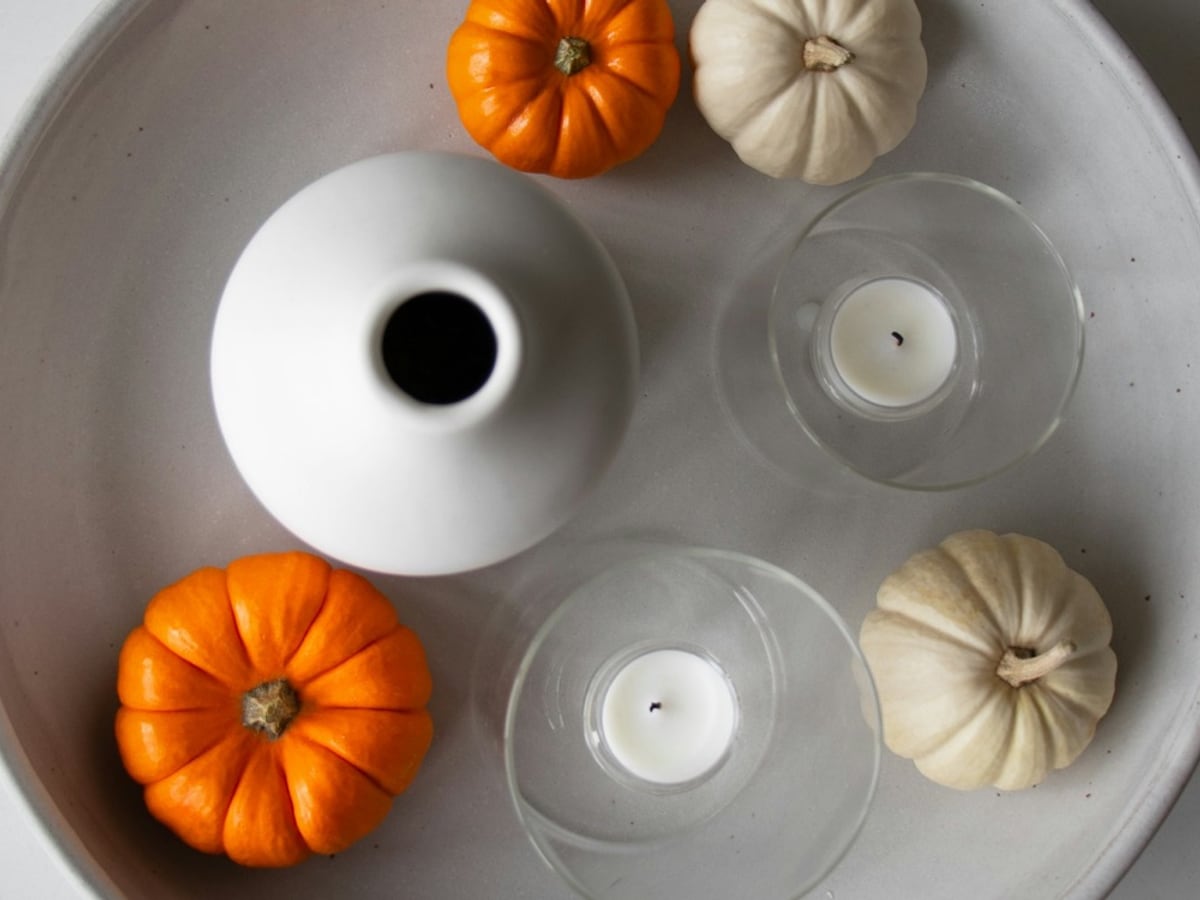 Orange and white miniature pumpkins arranged with glass candle holders on a round tray