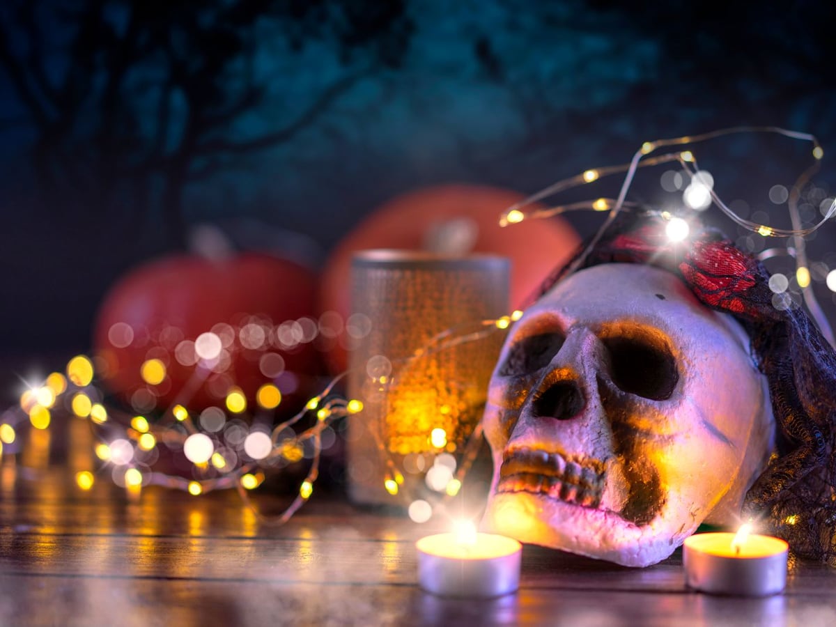A skull, pumpkins, candles and string lights arranged for Halloween