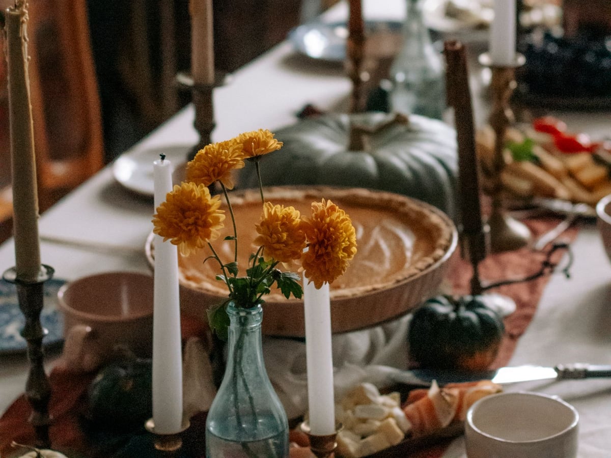 Candles, pumpkins and yellow flowers arranged across an autumn dining table