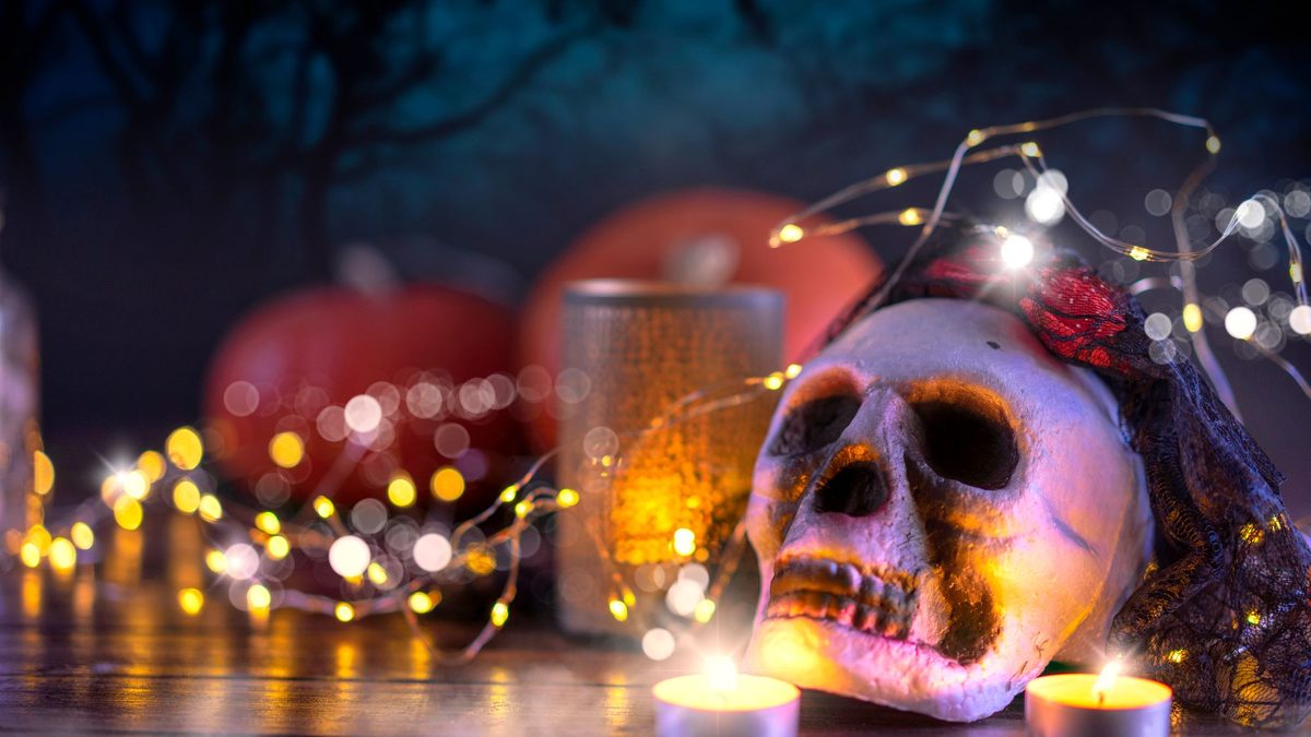 Skull, candles and string lights arranged with pumpkins indoors