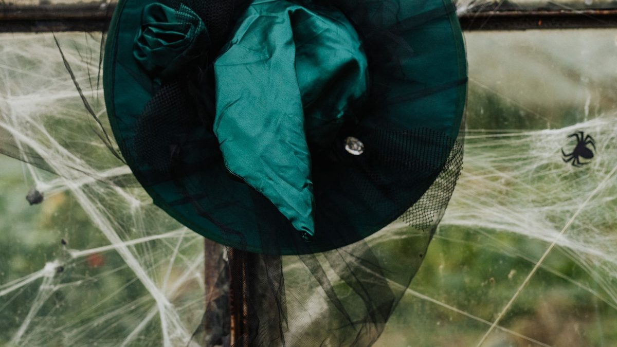 Green witch hat hanging from a cobweb-covered window