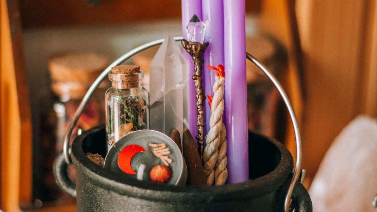 Black cauldron holding crystals beside purple candles and potion bottles