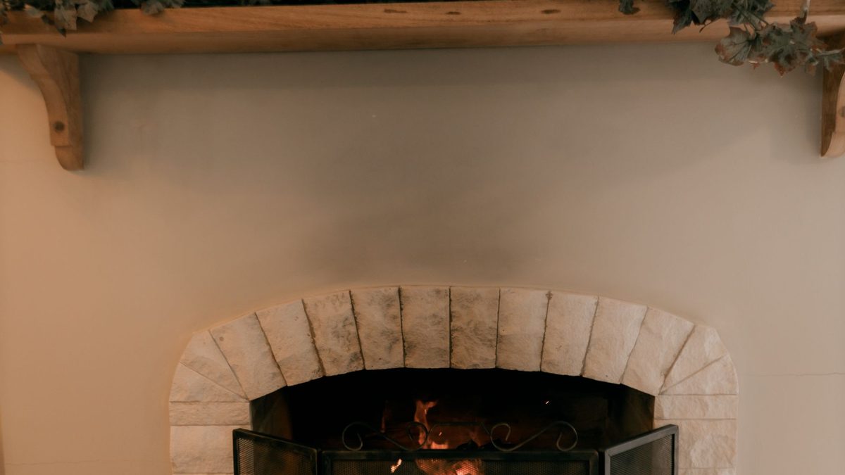 Green garland and wood candle holders arranged across a warm fireplace mantel
