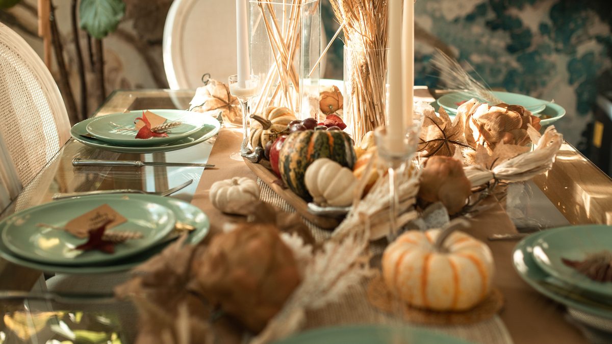 Green plates, wheat, pumpkins and place cards arranged on a Thanksgiving dinner table