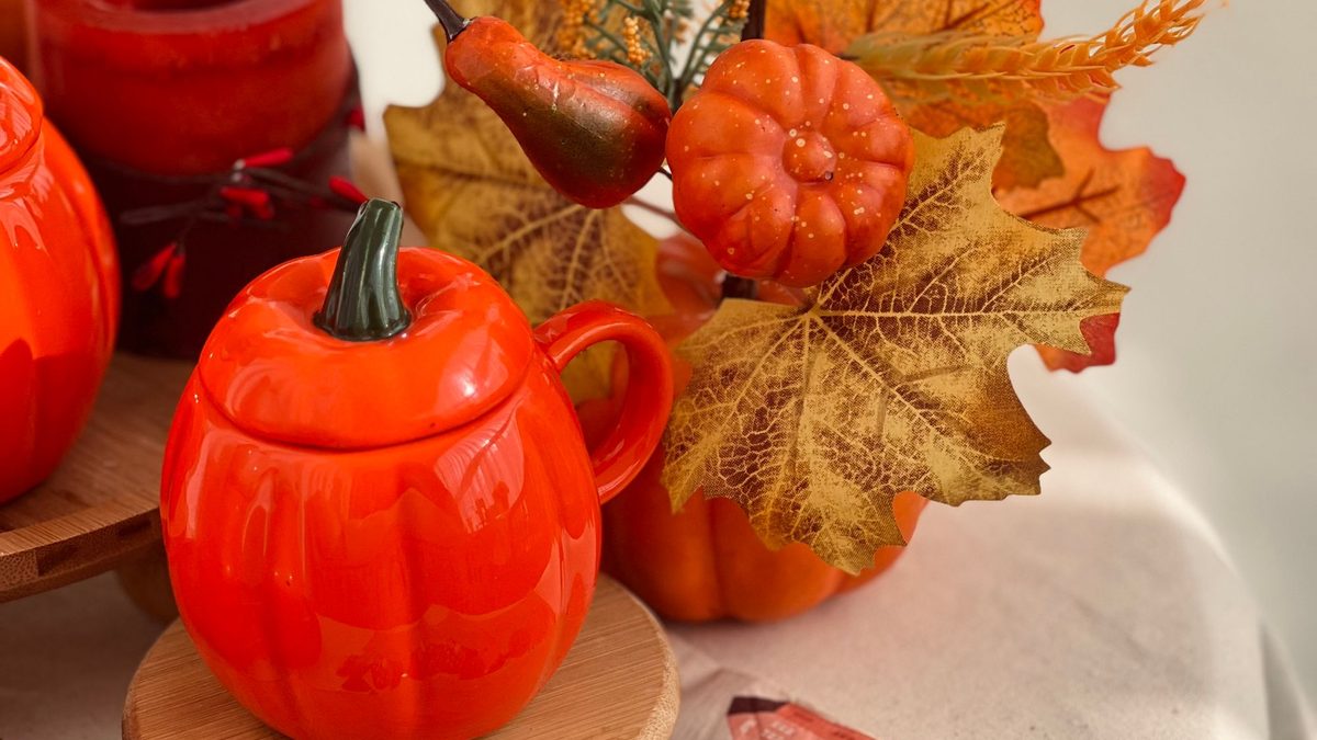 Orange pumpkin serveware, faux leaves and fall napkins arranged on a tabletop