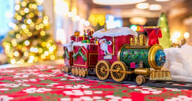 A red and green toy train beside a softly lit Christmas tree