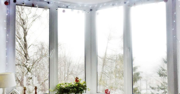 A bright corner window trimmed with white Christmas lights and hanging ornaments
