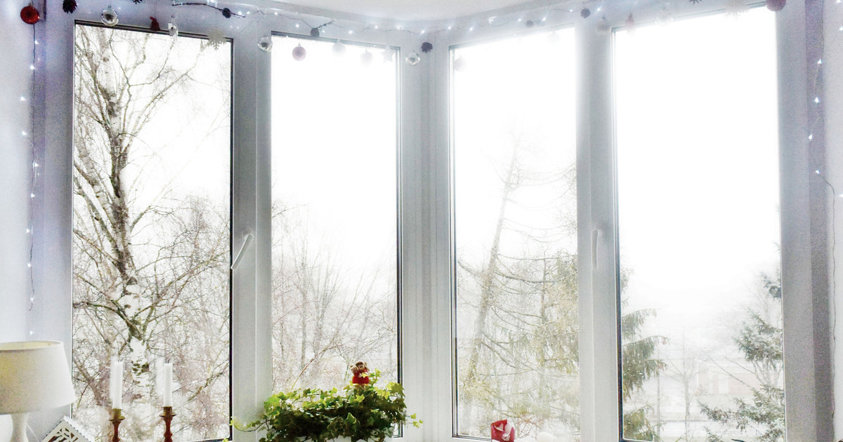 A bright corner window trimmed with white Christmas lights and hanging ornaments
